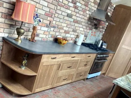 Shaker style cherry kitchen cabinets against an exposed brick wall, countertop still wrapped for protection